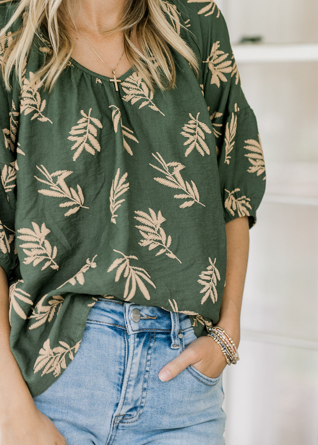 Model wearing an oversized hunter green top with wheat colored graphics, v-neck and short sleeves.