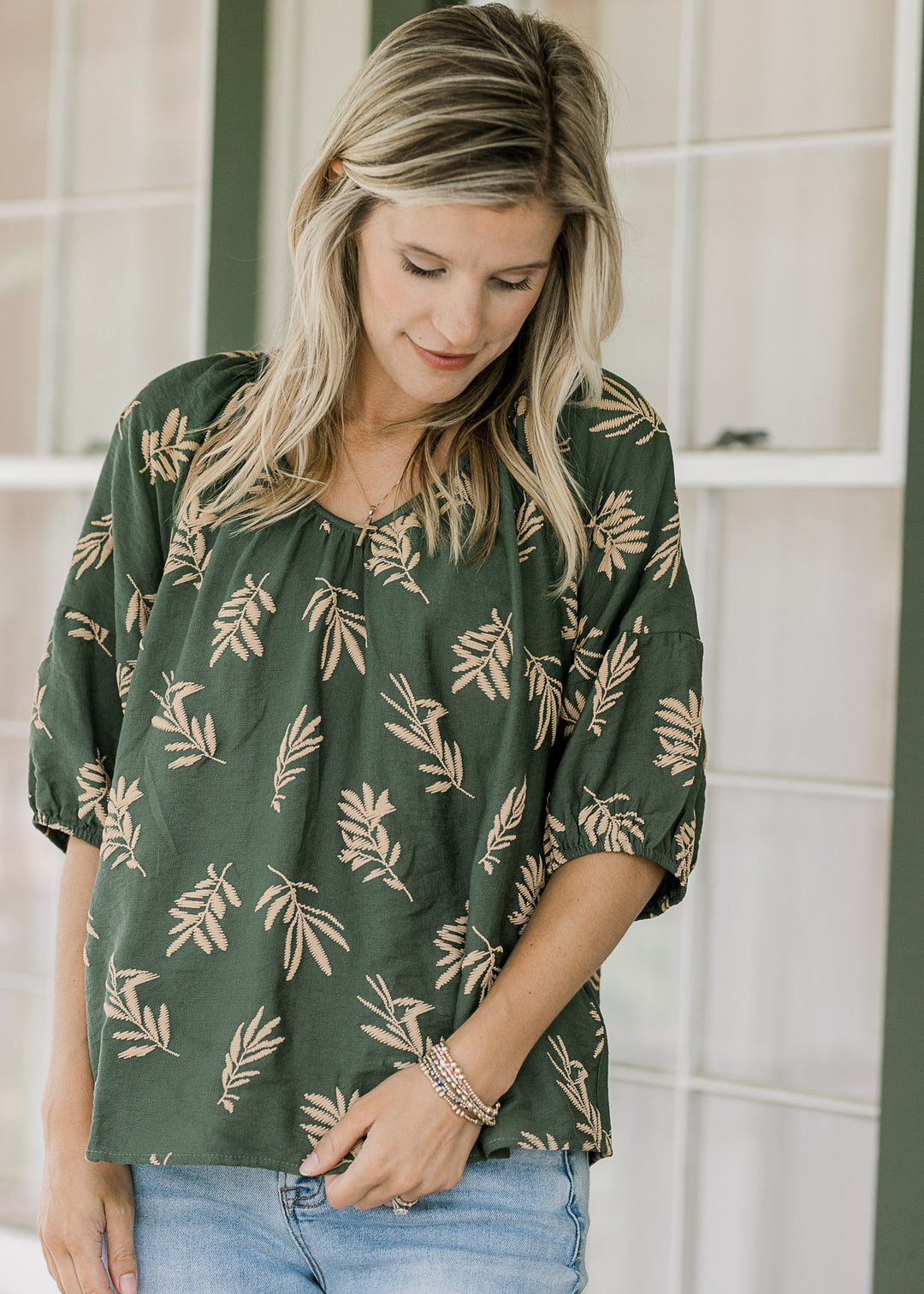 Model wearing a hunter green top with wheat colored graphics and short sleeves with elastic cuff.