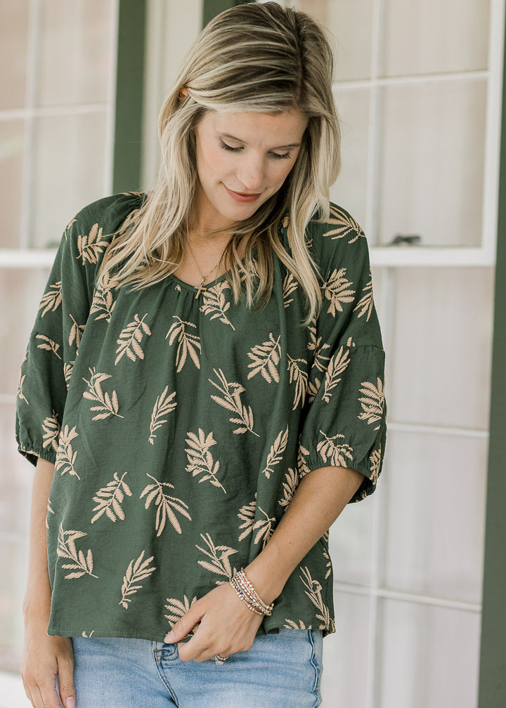 Model wearing a hunter green top with wheat colored graphics and short sleeves with elastic cuff.