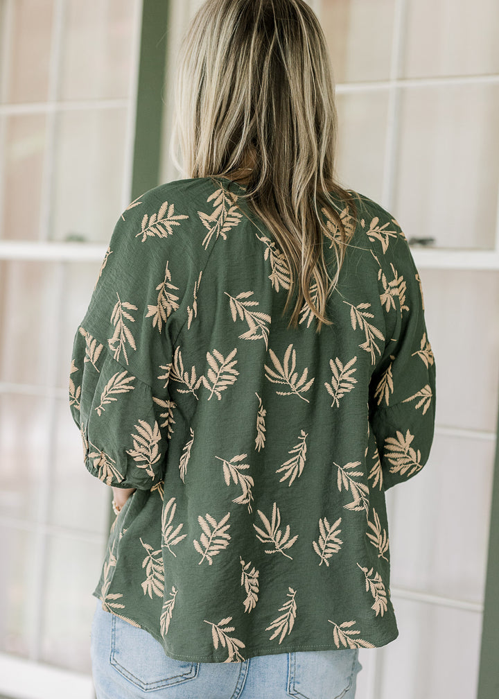 Back view of Model wearing a hunter green top with wheat colored graphics and short sleeves.