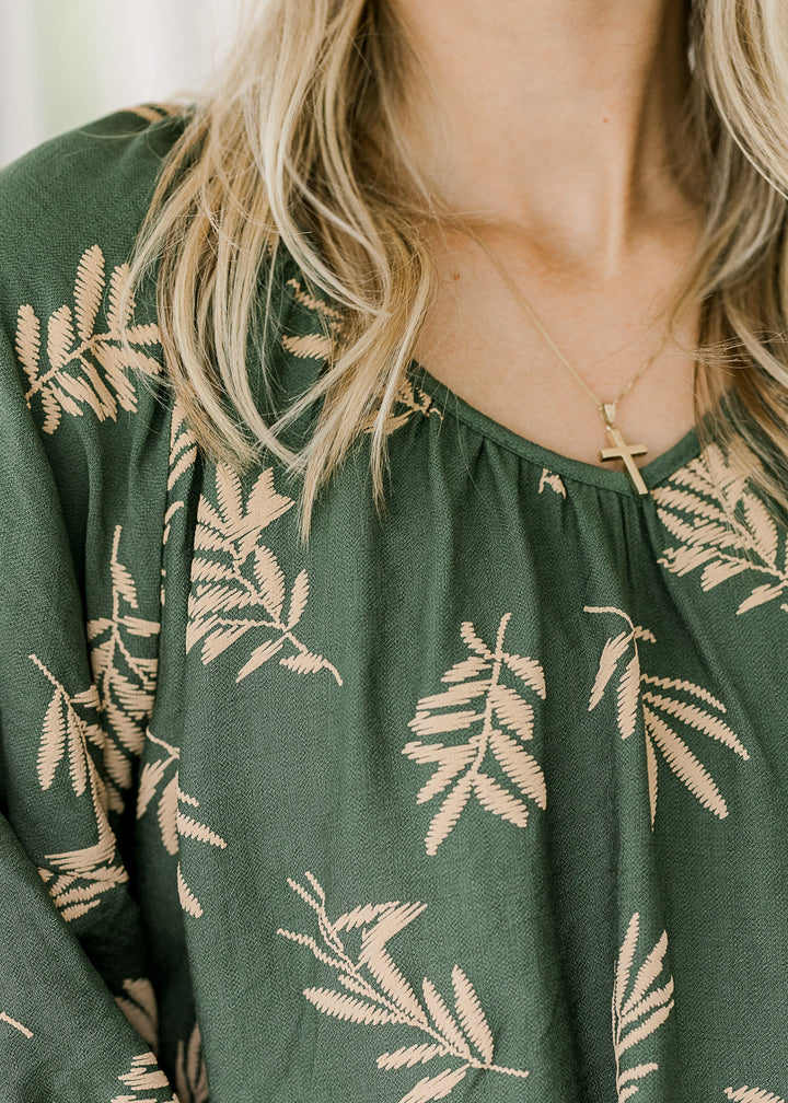 Close up of v-neck and wheat colored graphic on a hunter green short sleeve blouse. 