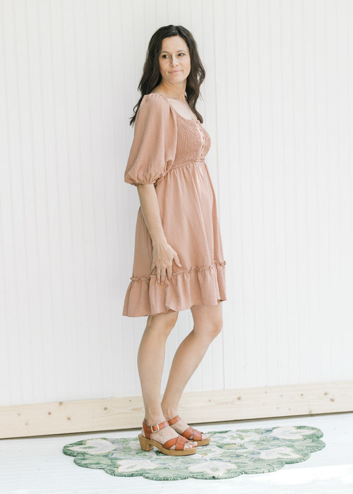 Model wearing an above the knee dusty mauve dress with a smocked bodice and bubble short sleeves.