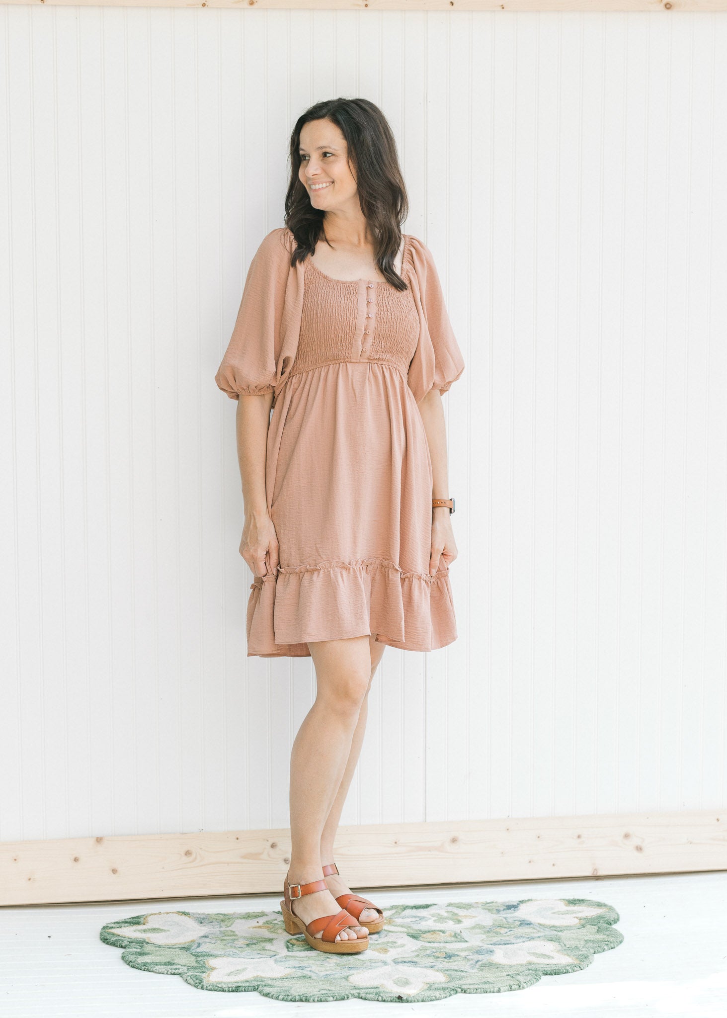 Model wearing sandals with a mauve dress with a smocked bodice and bubble short sleeves.