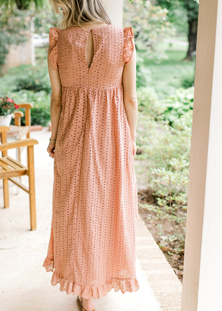 Back view of Model wearing a coral maxi with eyelets, ruffle at sleeve, keyhole and pockets. 