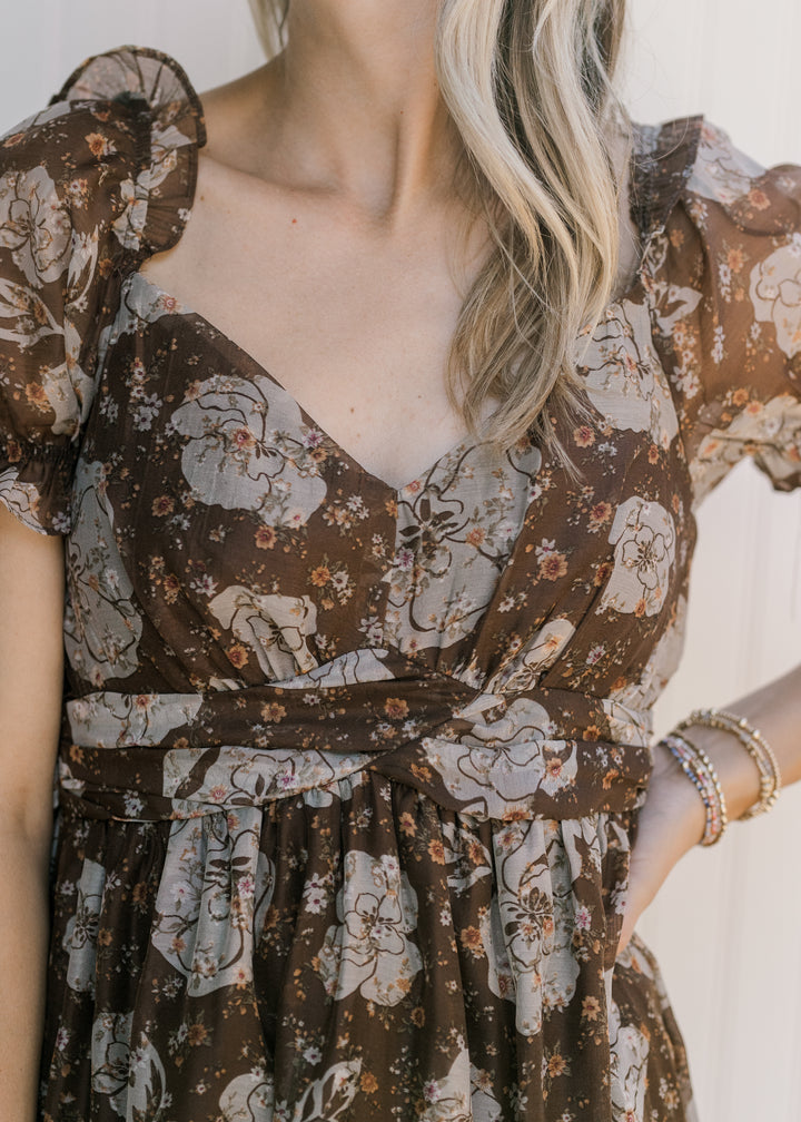 Close up of v-neck and sheer puff short sleeves on a brown midi with cream floral and a tie waist. 