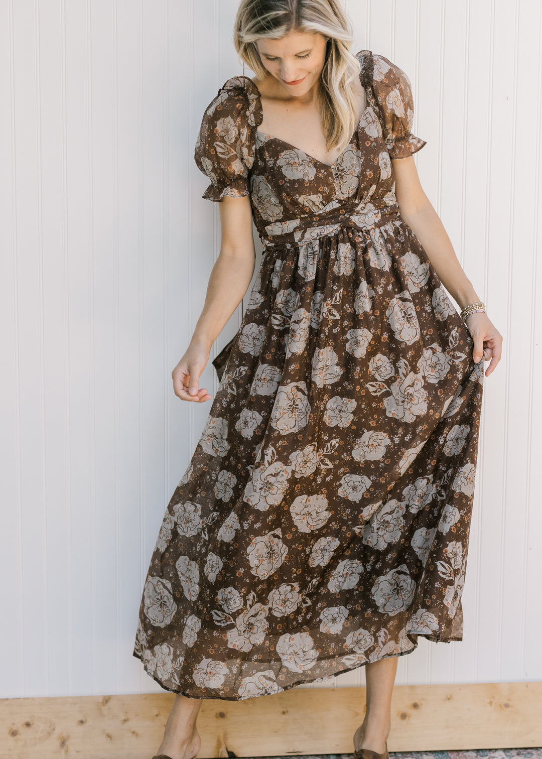 Model wearing a brown dress with cream floral, v-neck, full lining and sheer bubble short sleeves. 
