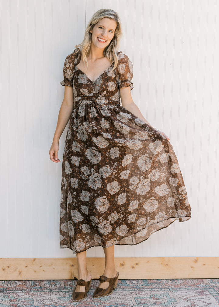 Model wearing heels and a brown midi with cream floral, v-neck and a smocked back with tie. 