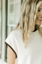 Close up of extended shoulder cap sleeve on a cream sweater with brown trim. 