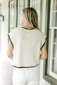 Back view of Model wearing a cream sweater with brown trim, cap sleeves.