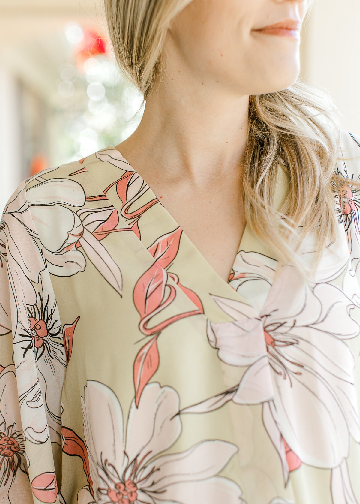 Close up of v-neck on a pale lime top with cream and coral floral and sheer 3/4 sleeves. 
