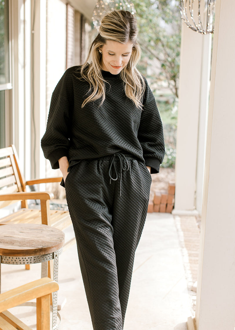 Model wearing a textured black two piece set with hands in pockets and top tucked in.