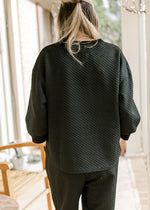 Back view of model in a black textured top with 3/4 sleeves and round neck with matching pants.