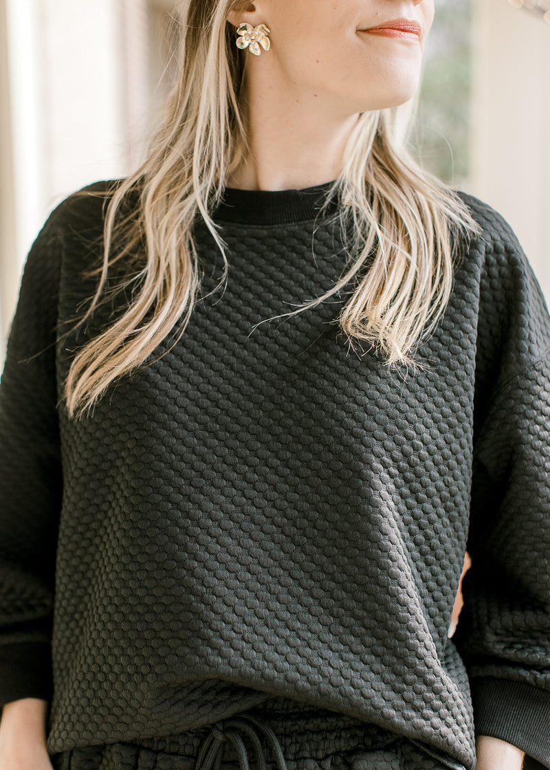 Model in a black textured top with 3/4 sleeves and round neck with matching pants.