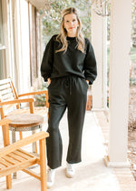 Model wearing a black set, top has 3/4 sleeves and a round neck, bottoms are wide leg and tie.