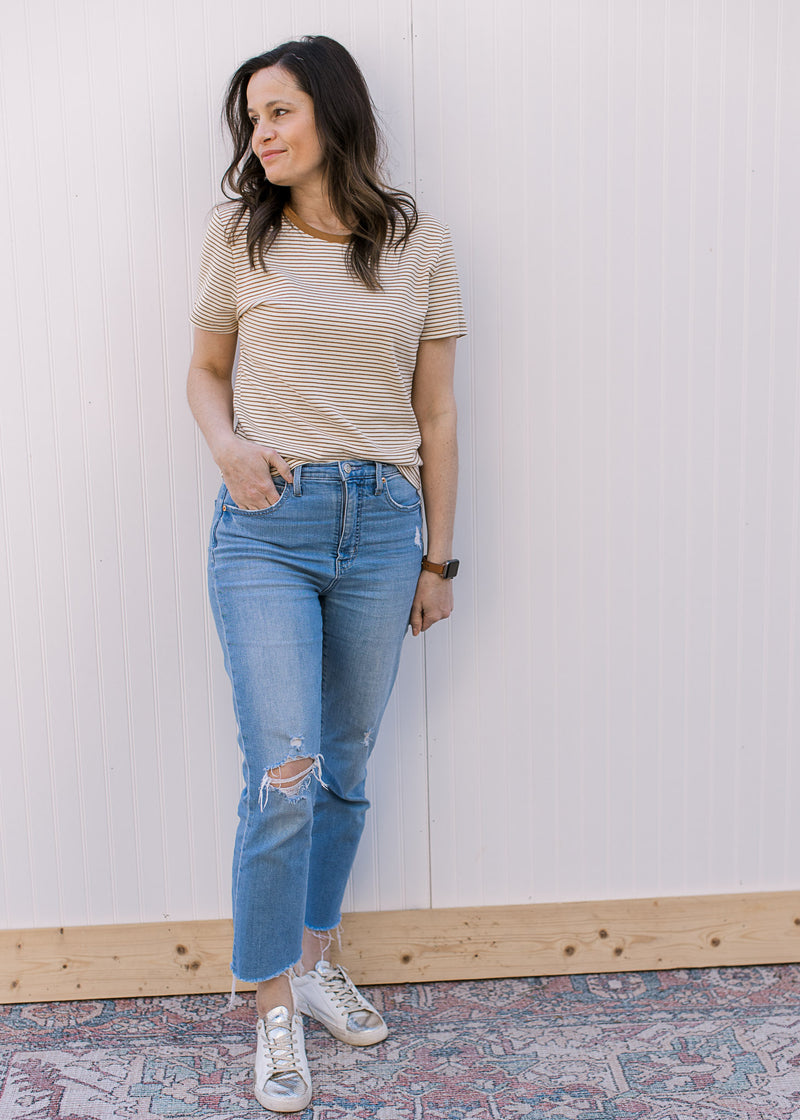 Model wearing jeans and a ecru and camel crew neck tee with stripes and short sleeves. 