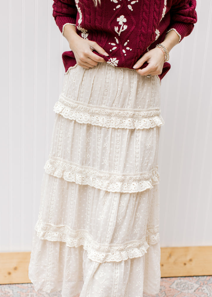 Model wearing a beige midi length skirt with an embroidered floral overlay and tiered ruffles. 