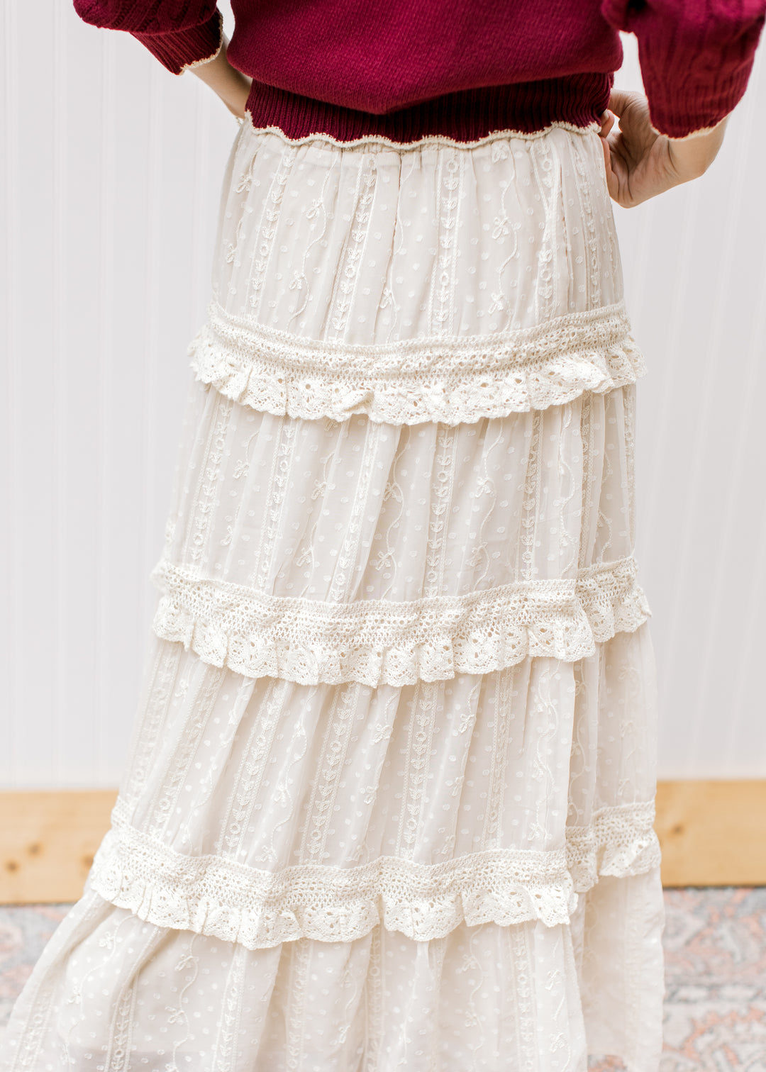 Back view of Model wearing a beige midi length skirt with an embroidered floral and tiered ruffles. 