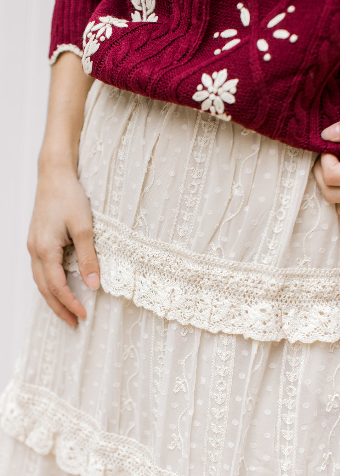 Close up of embroidered floral and tiered ruffles on a beige midi skirt with an elastic waist. 