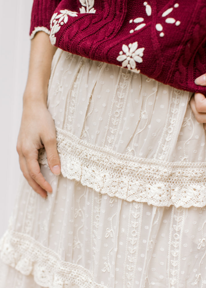 Close up of embroidered floral and tiered ruffles on a beige midi skirt with an elastic waist. 