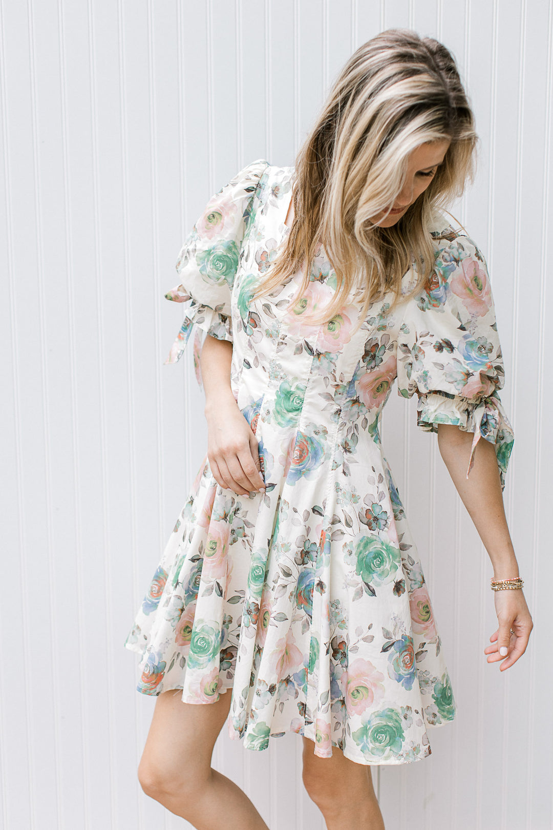Model wearing a cream above the knee dress with watercolor floral and pleated bodice. 