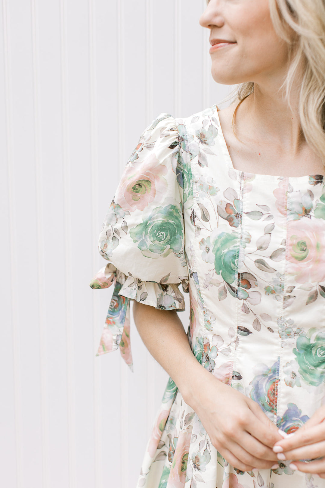 Close up of square neck and puff short sleeve with a tie on a cream dress with watercolor floral. 