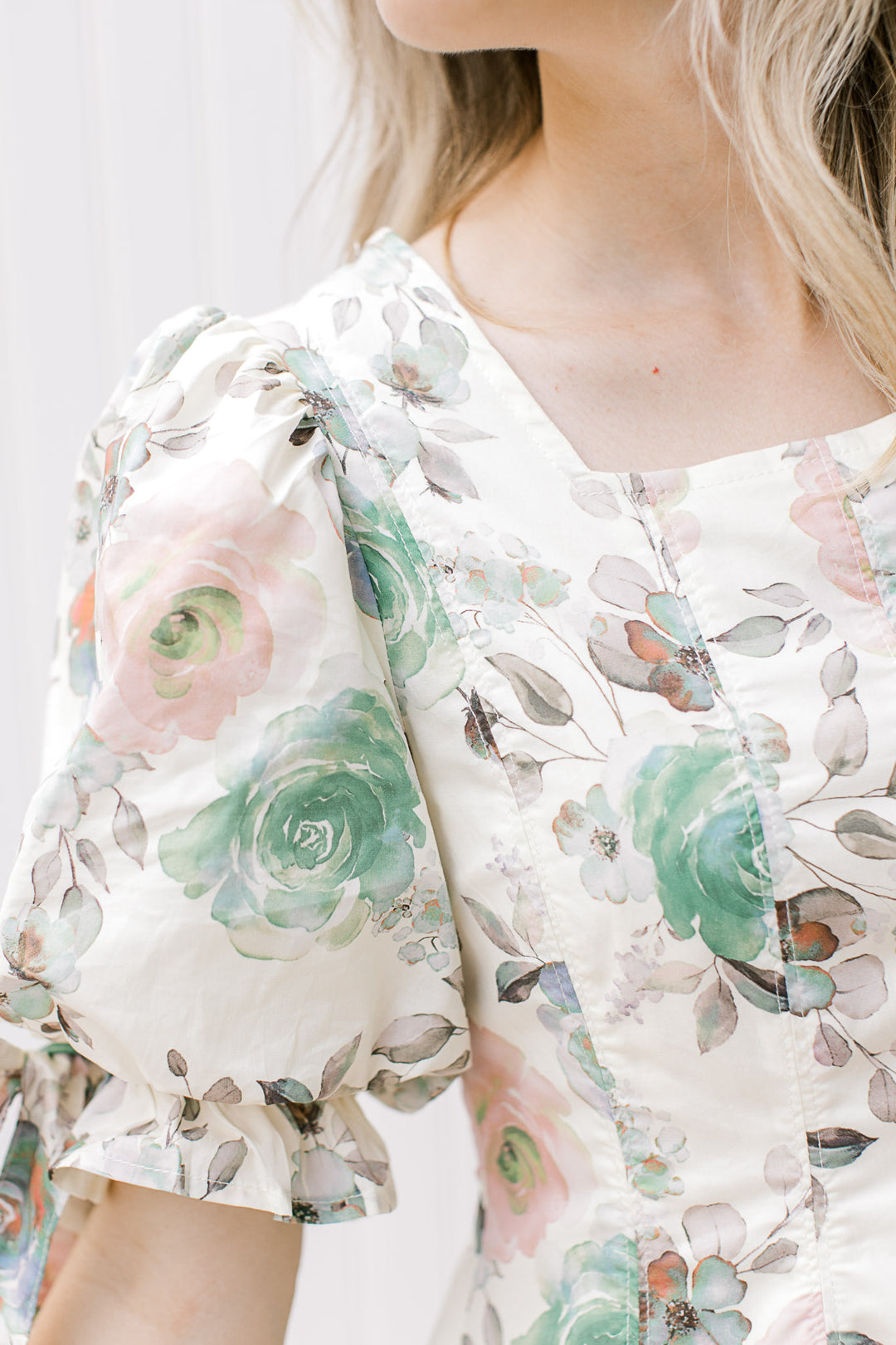 Close up of square neck and pleated shoulder on a short sleeve cream dress with flowers. 