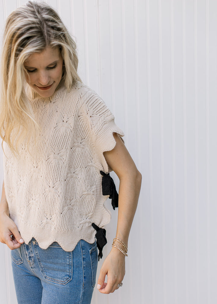Model wearing an oatmeal crochet top with scallop edging and tie side closure.