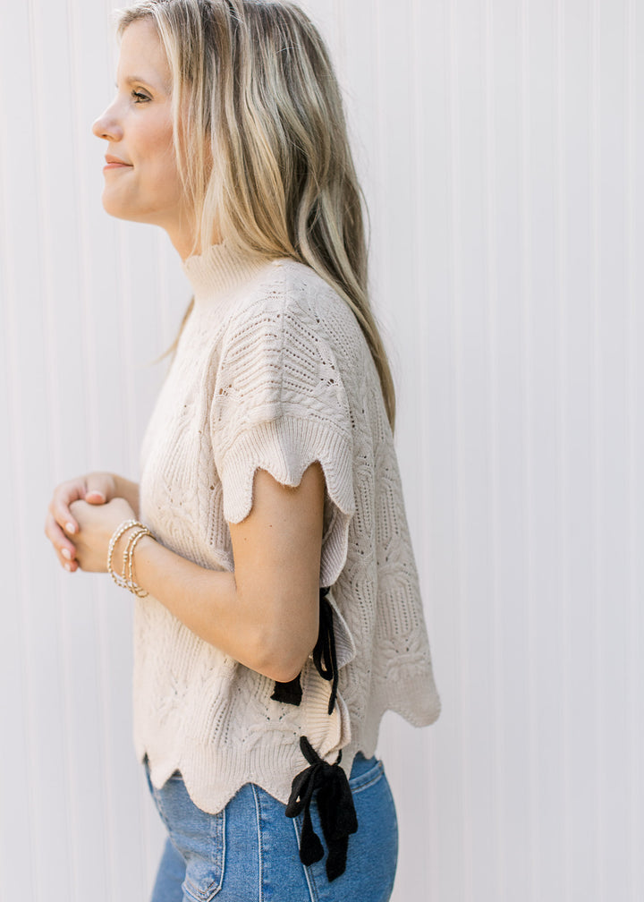 Model wearing an oatmeal knit short sleeve sweater with a mock neck and tie sides.