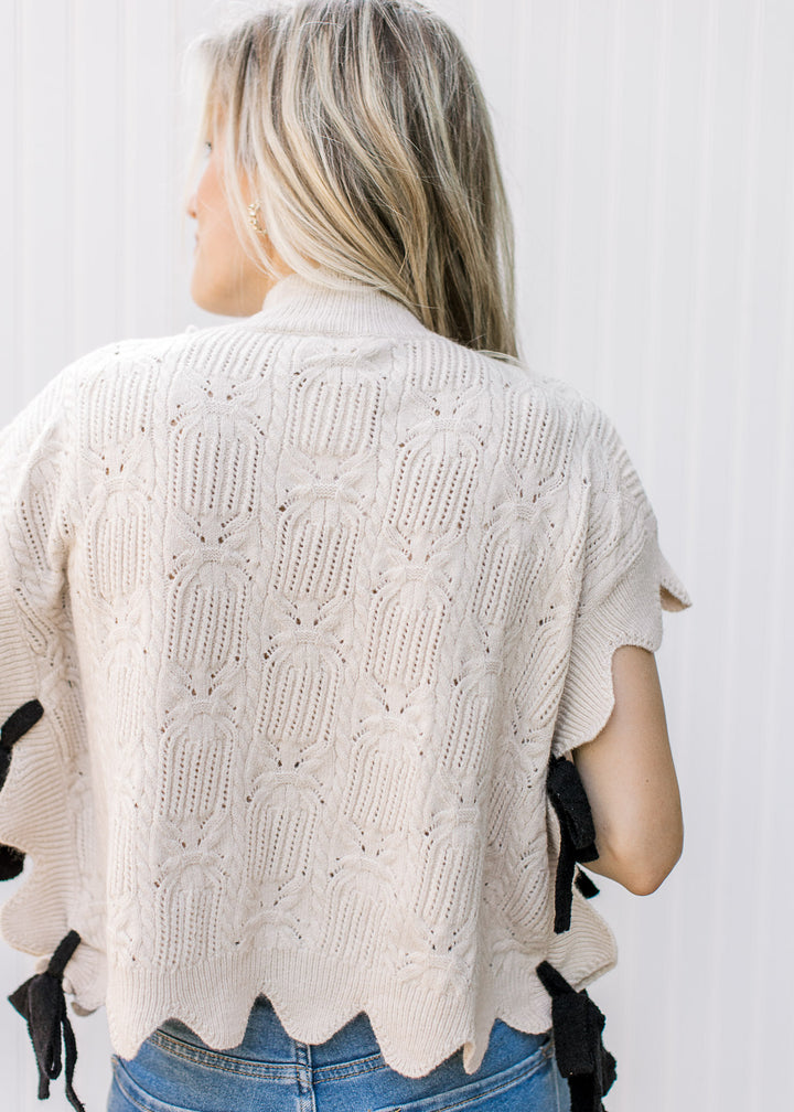 Back view of model wearing an oatmeal knit sweater with scalloped edges. 