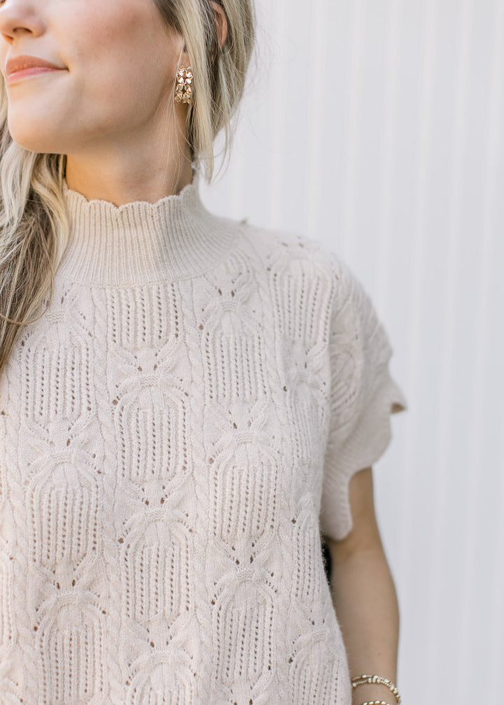 Close up of scalloped mock neck on a short sleeve oatmeal knit sweater with scalloped edges.