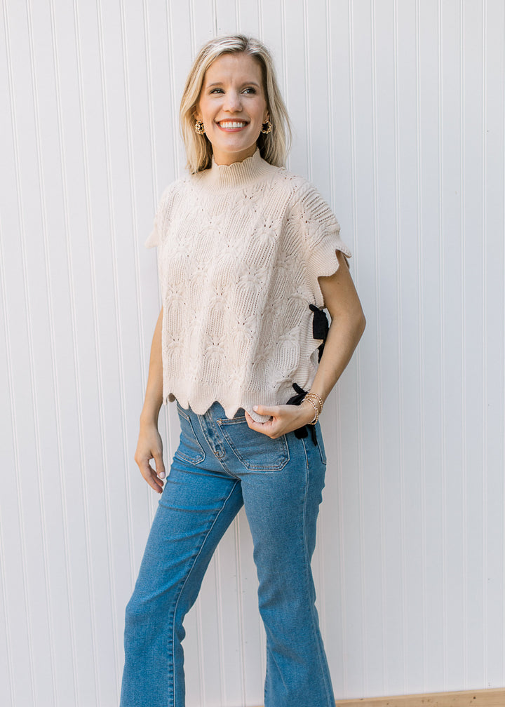 Model wearing jeans with an oatmeal knit short sleeve sweater with black side tie closure.