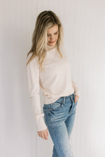 Model wearing jeans with a lightweight cream sweater with long sleeves and a mock neckline.