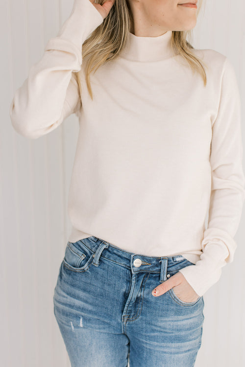 Model wearing a lightweight cream sweater with long sleeves and a mock neckline. 