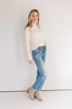 Model wearing jeans, booties and a lightweight cream sweater with long sleeves and a mock neckline.