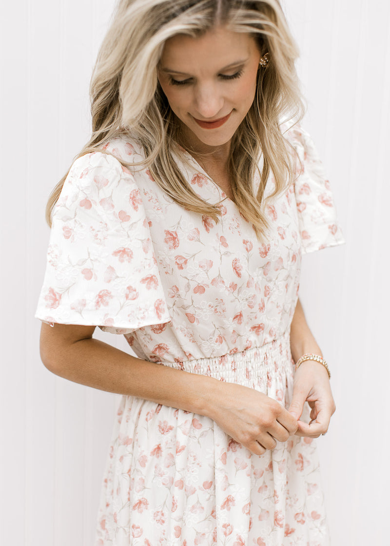Close up of short sleeve, v-neck and elastic waist on a white maxi with embroidered flowers.