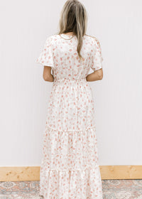 Back view of Model wearing a white v-neck maxi with pale pink embroidered floral and elastic waist.