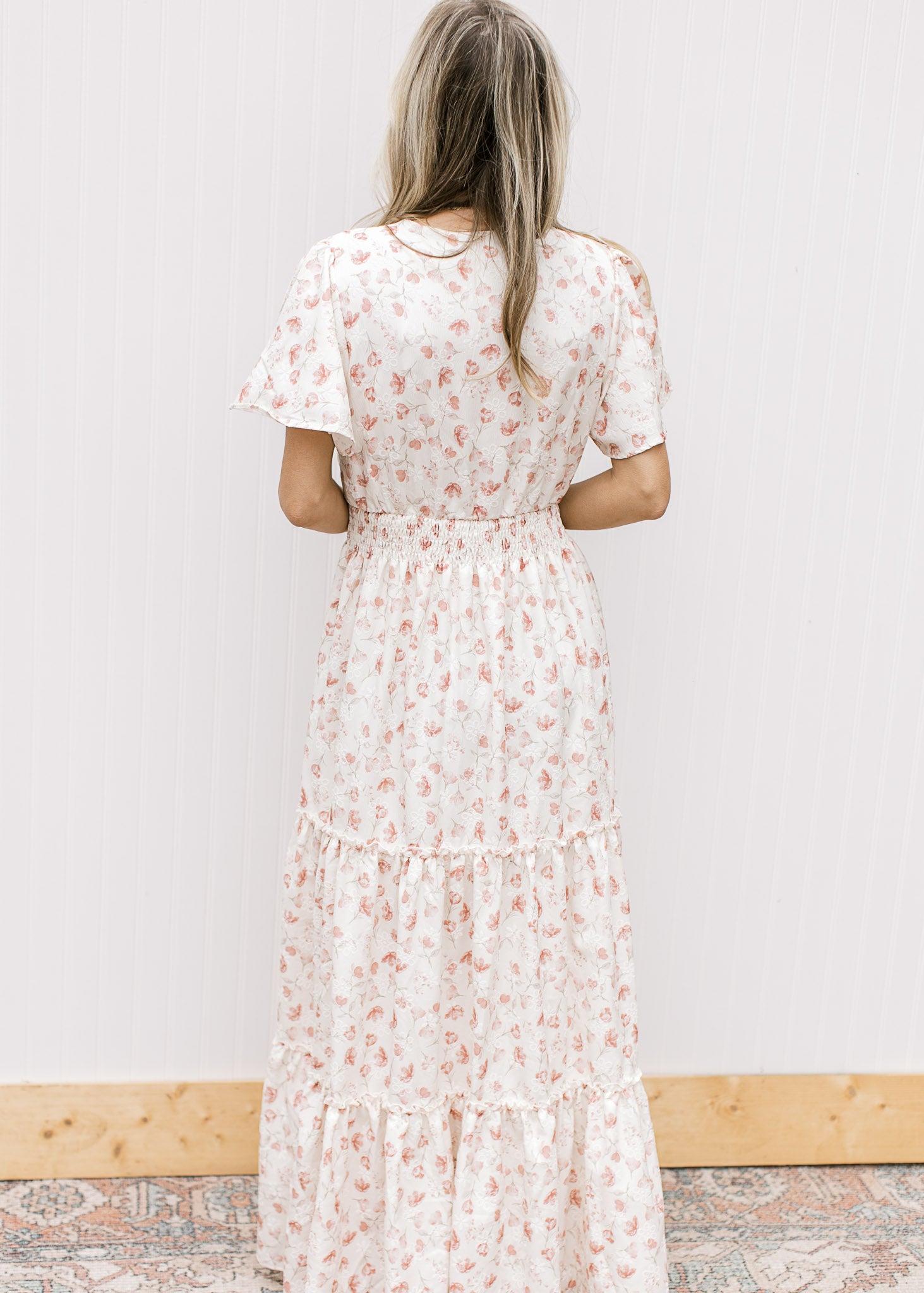 Back view of Model wearing a white v-neck maxi with pale pink embroidered floral and elastic waist.