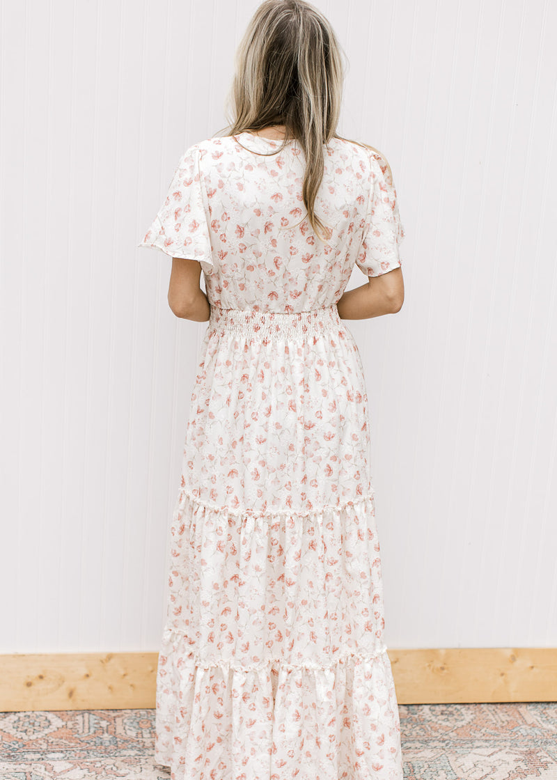 Back view of Model wearing a white v-neck maxi with pale pink embroidered floral and elastic waist.