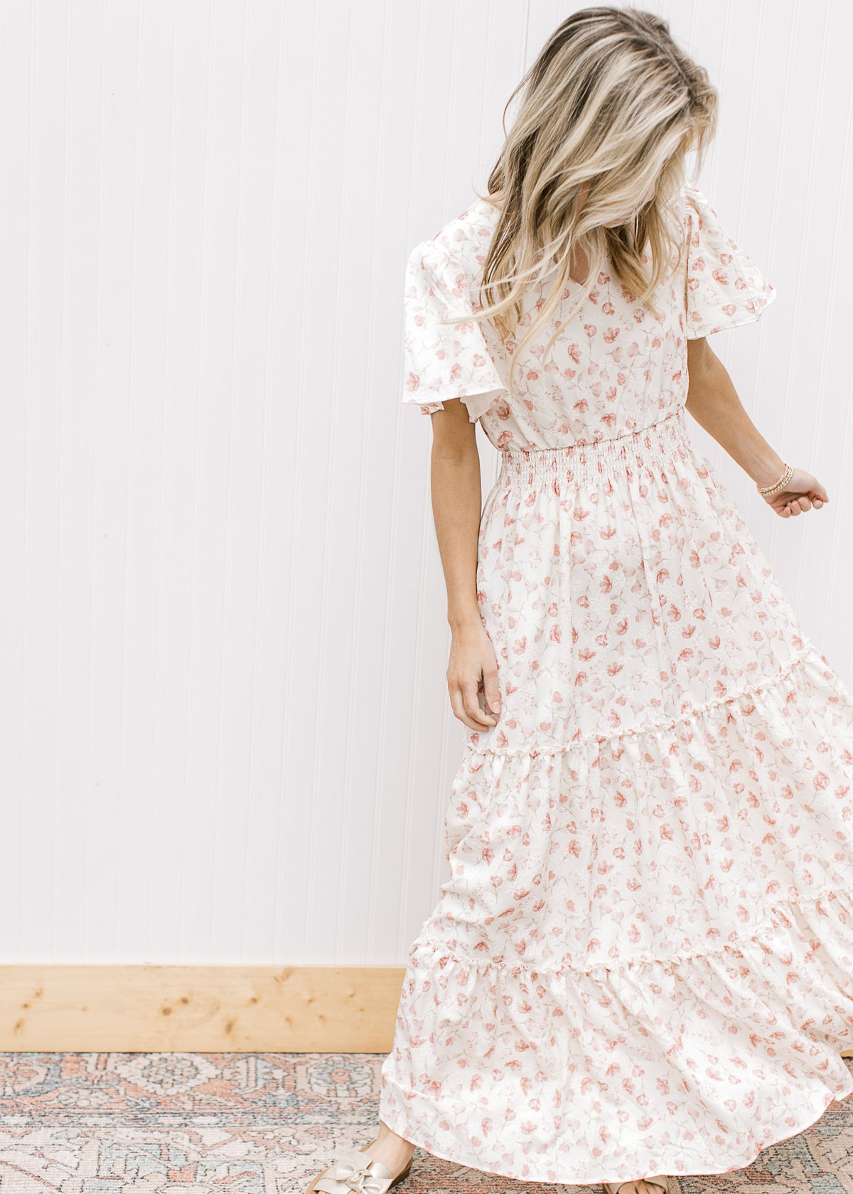 Model wearing a white v-neck maxi with pale pink embroidered floral, short sleeves and tiers.