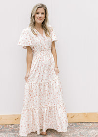 Model wearing sandals and a white v-neck maxi with pale pink embroidered floral and elastic waist.