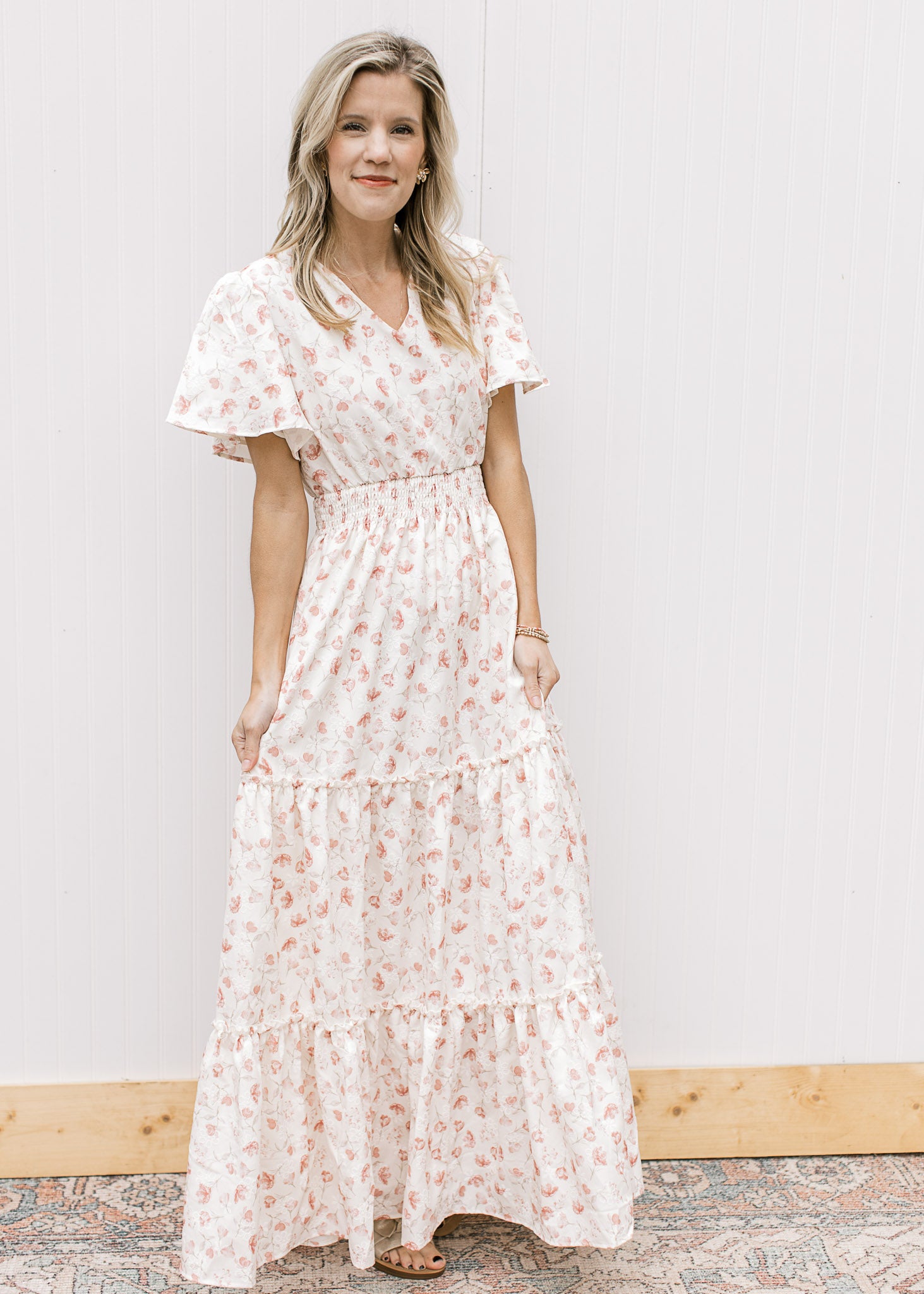 Model wearing sandals and a white v-neck maxi with pale pink embroidered floral and elastic waist.