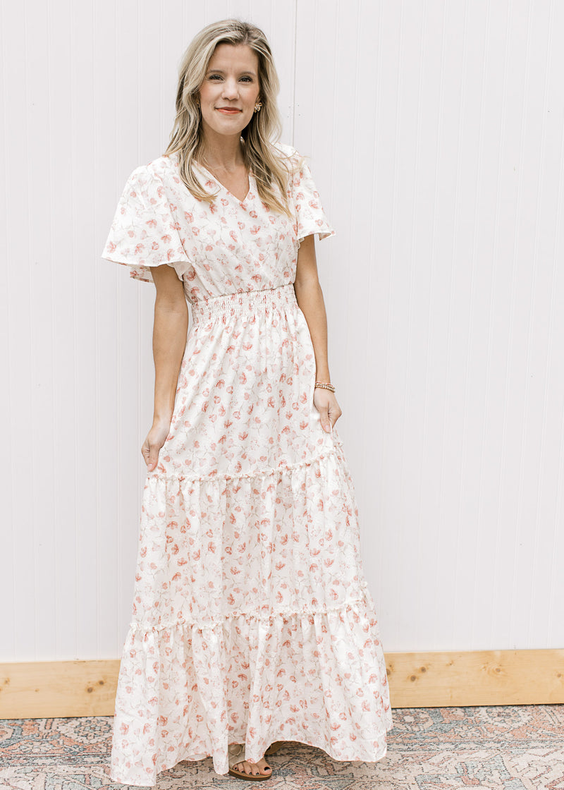Model wearing sandals and a white v-neck maxi with pale pink embroidered floral and elastic waist.