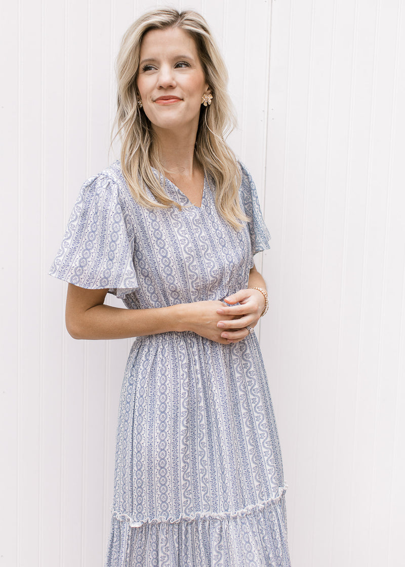Close up of v-neck and short sleeves on a white maxi with a pale blue print and tired skirt. 