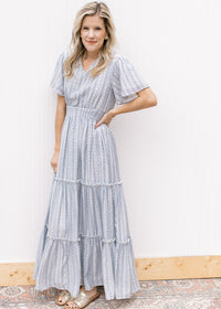 Model wearing sandals and a tiered white maxi with a pale blue print and a wide elastic waist. 