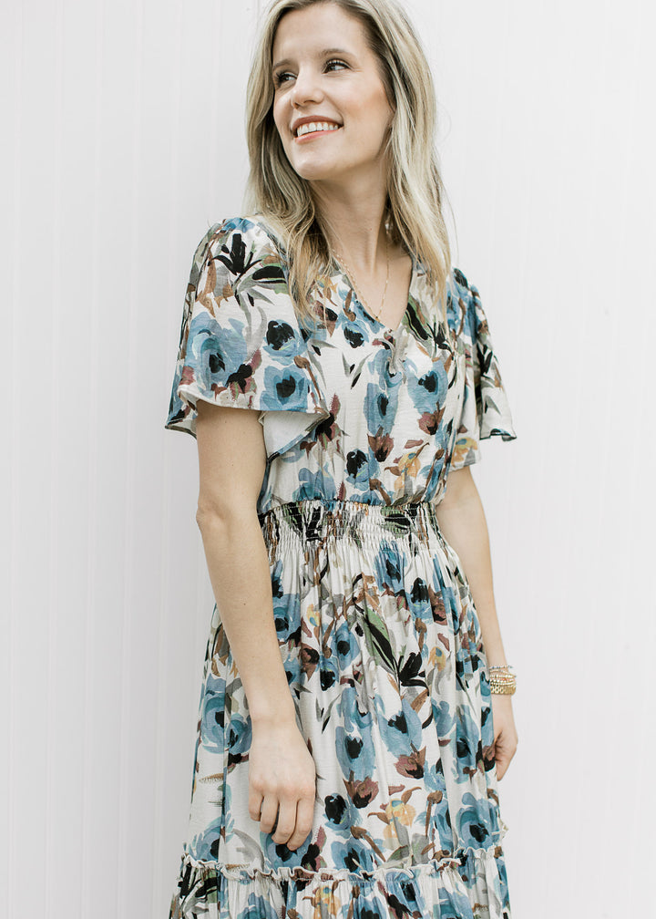 Close up of elastic waist, v-neck and flutter short sleeves on a cream mid with watercolor floral.