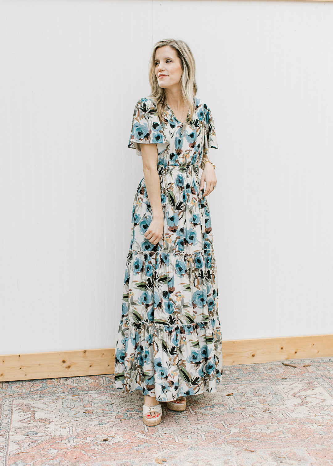 Model wearing a cream maxi with watercolor floral, flutter short sleeves, tiers and elastic waist.