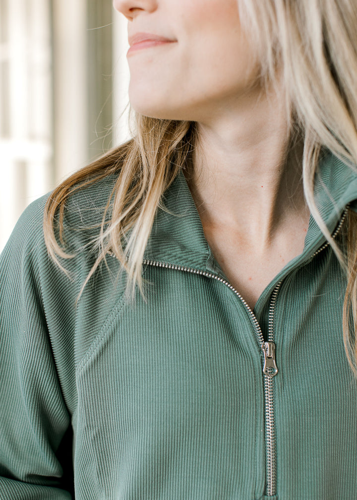 Close up of collar and quarter zip on a dark green long sleeve pullover with a ribbed material.