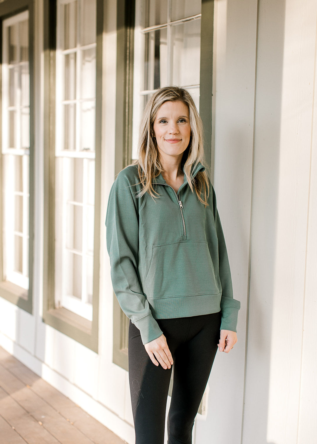 Model wearing leggings and a dark green ribbed pullover with front pouch pocket and long sleeves. 