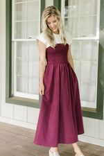 Model wearing a plum dress with a white yolk, smocked bodice and cap short sleeves.