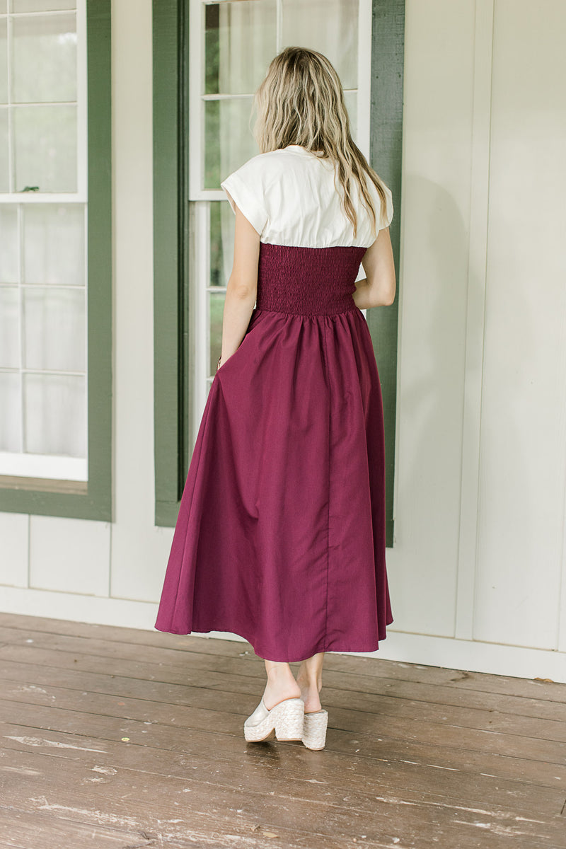 Back view of a plum midi with a smocked bodice and white yolk with cap short sleeves.